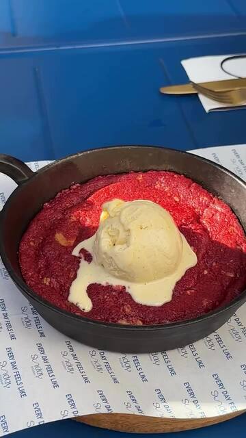 O papel dos tabuleiros, com «Every day feels like» e o logótipo da casa repetidos, debaixo de uma frigideira com uma cookie red velvet e uma bola de gelado.