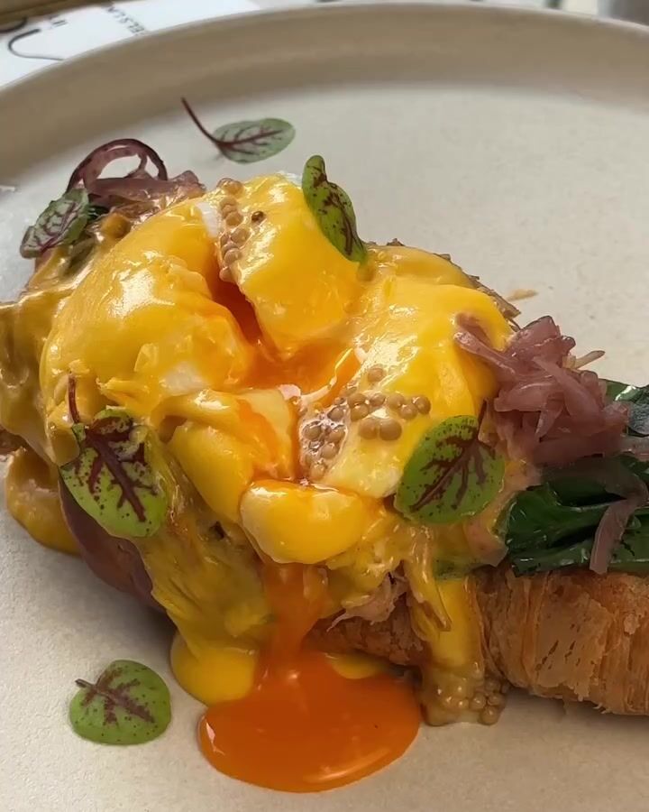 Ovos Benedict com molho holandês, a gema a escorrer, cebola roxa e rebentos.